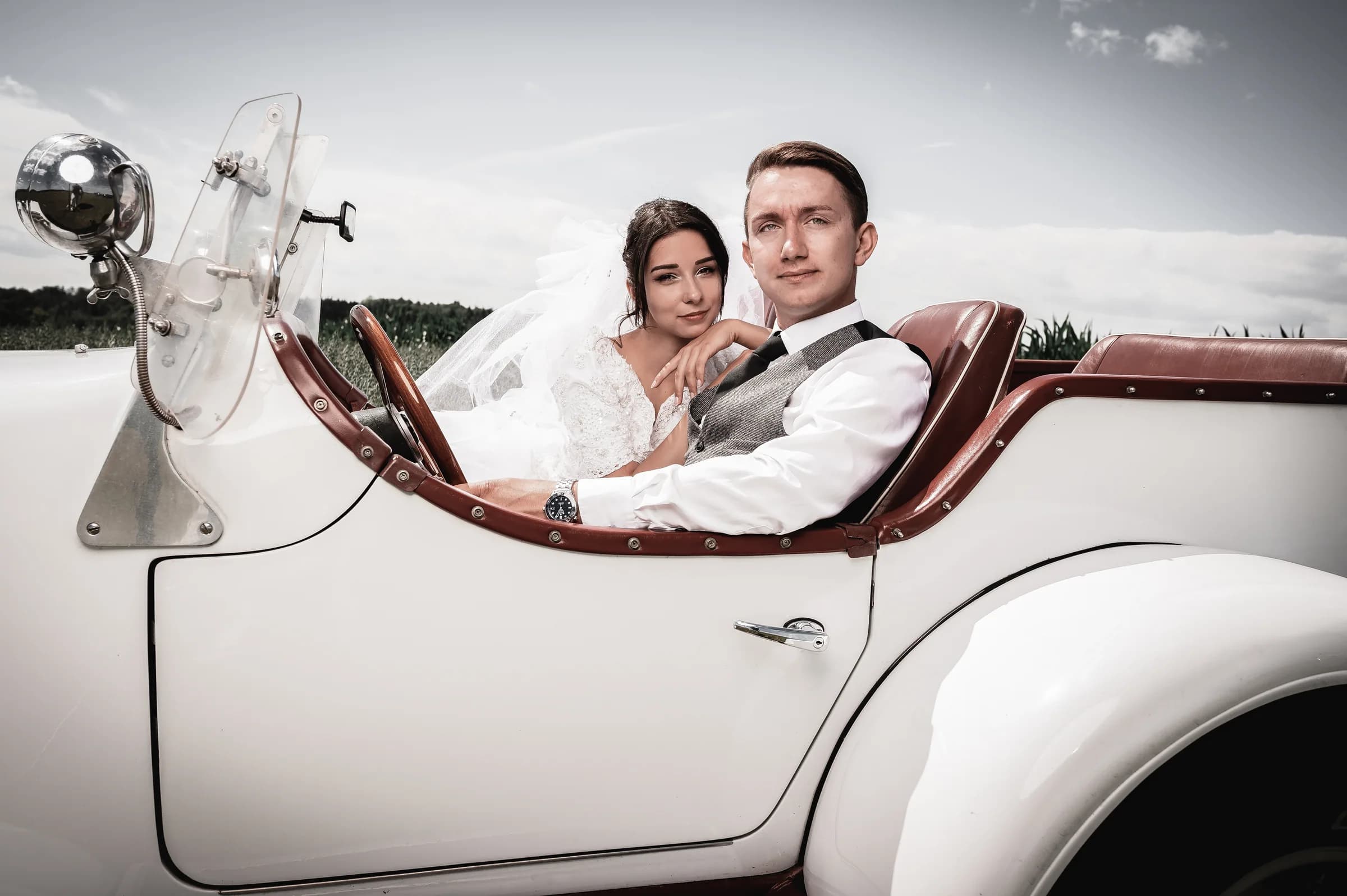 Brautpaar im weißen Oldtimer-Cabrio vor weitem Himmel