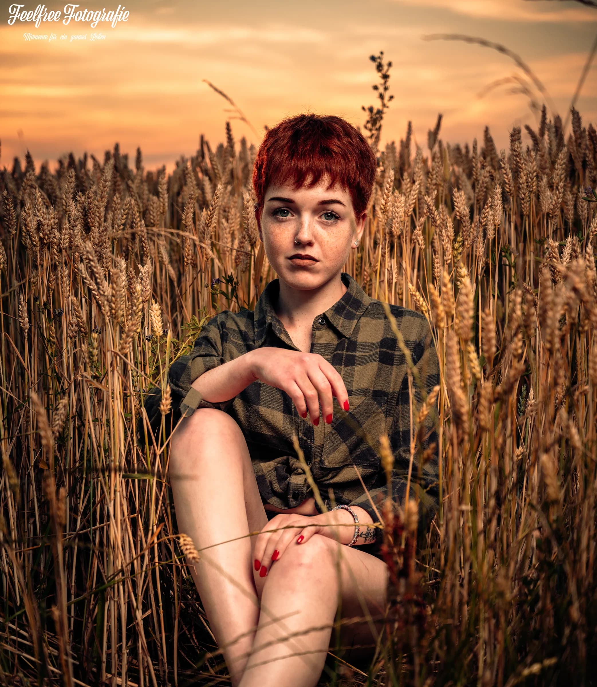 Frau mit roten Haaren sitzt im Kornfeld bei Sonnenuntergang
