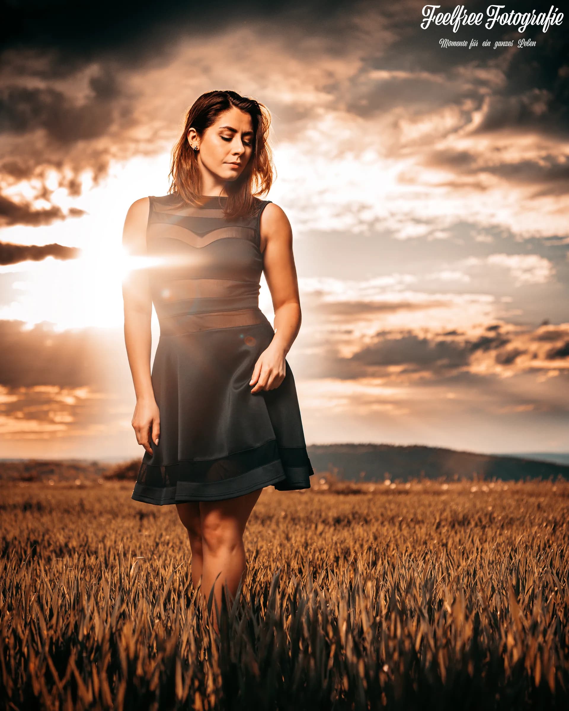 Frau im schwarzen Kleid vor dramatischem Wolkenhimmel über dem Feld