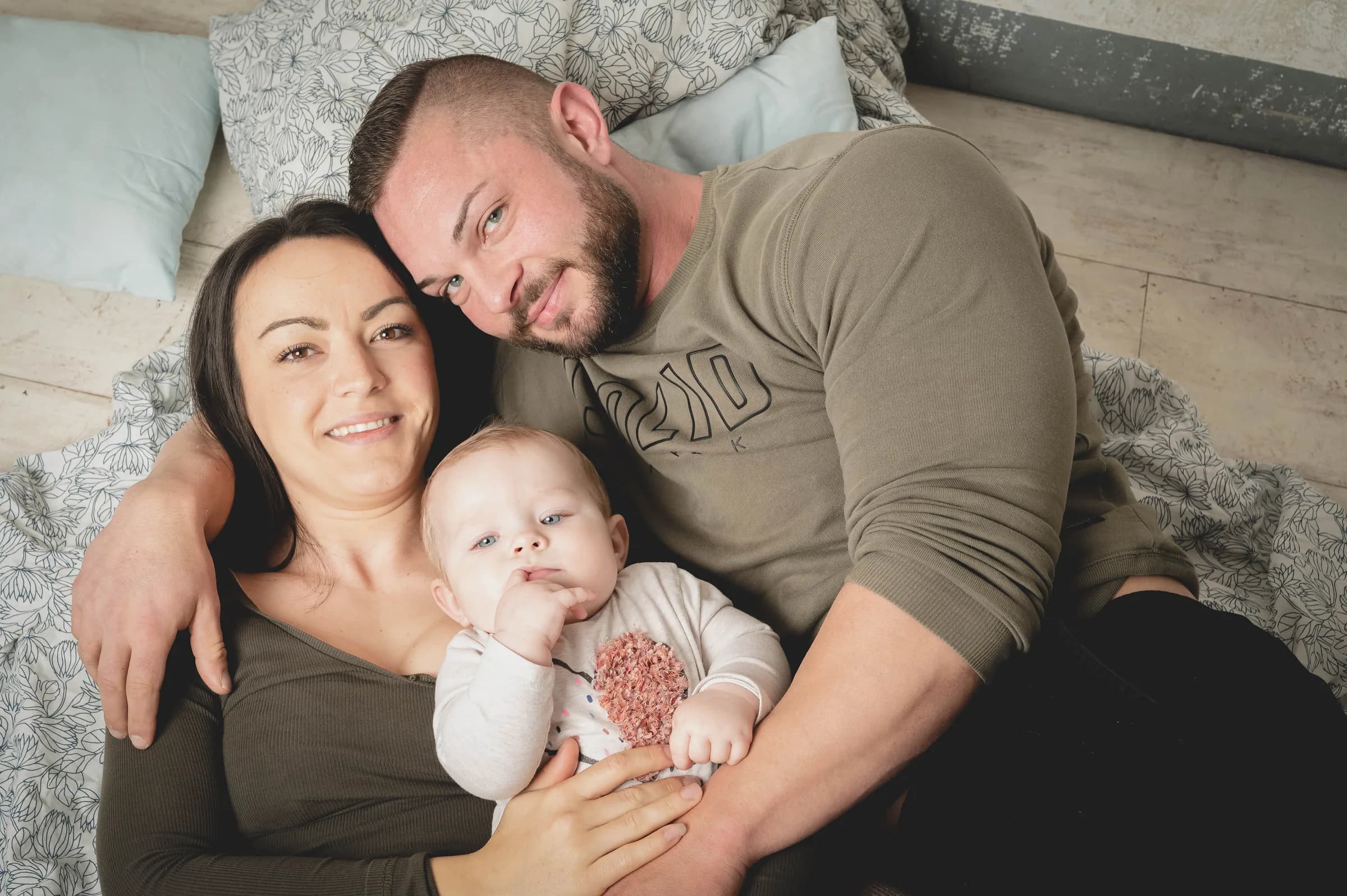 Eltern liegen mit ihrem Baby auf einer Decke und lachen in die Kamera