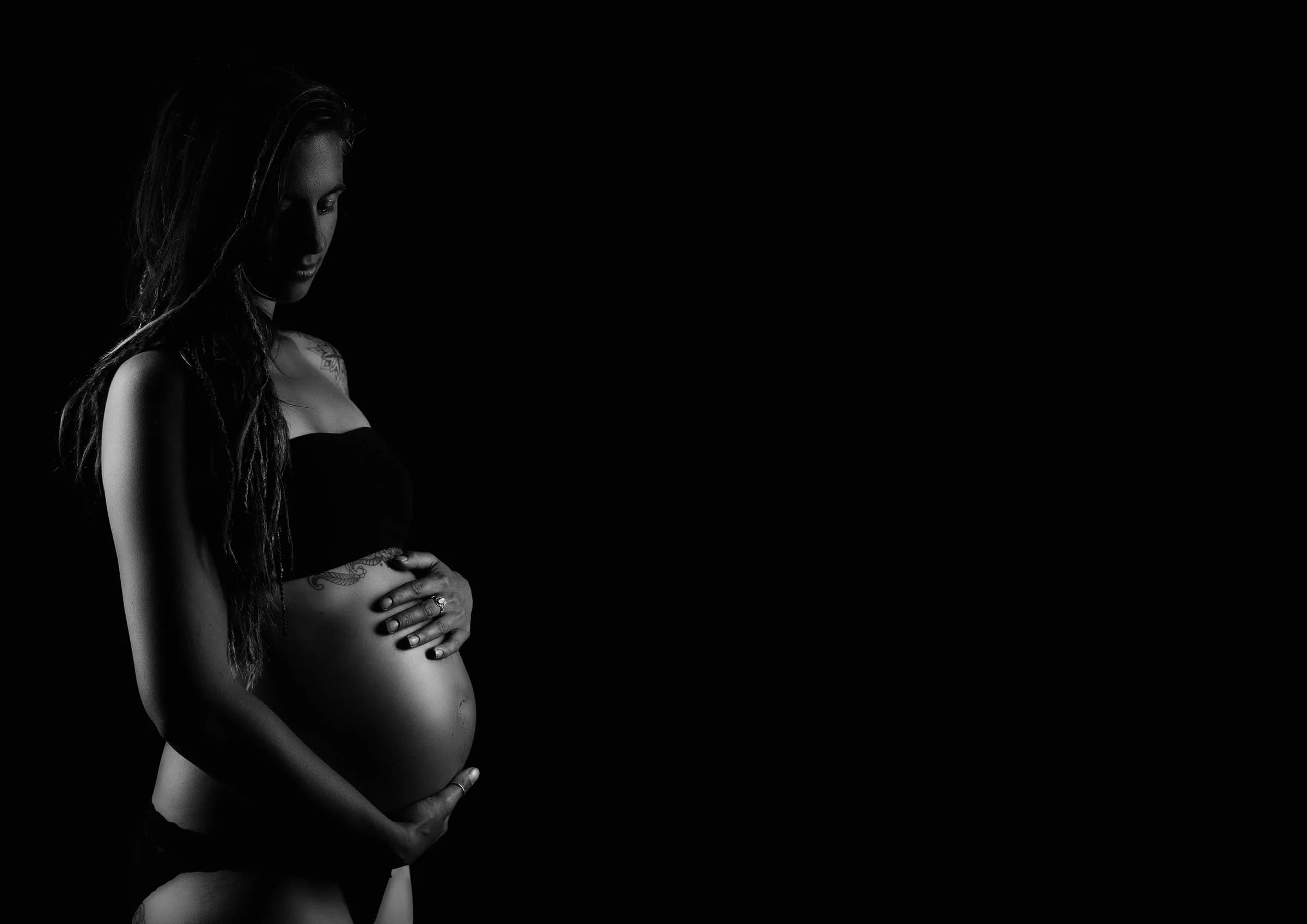 Schwangere hält ihren Bauch, Schwarz-Weiß mit weichem Licht
