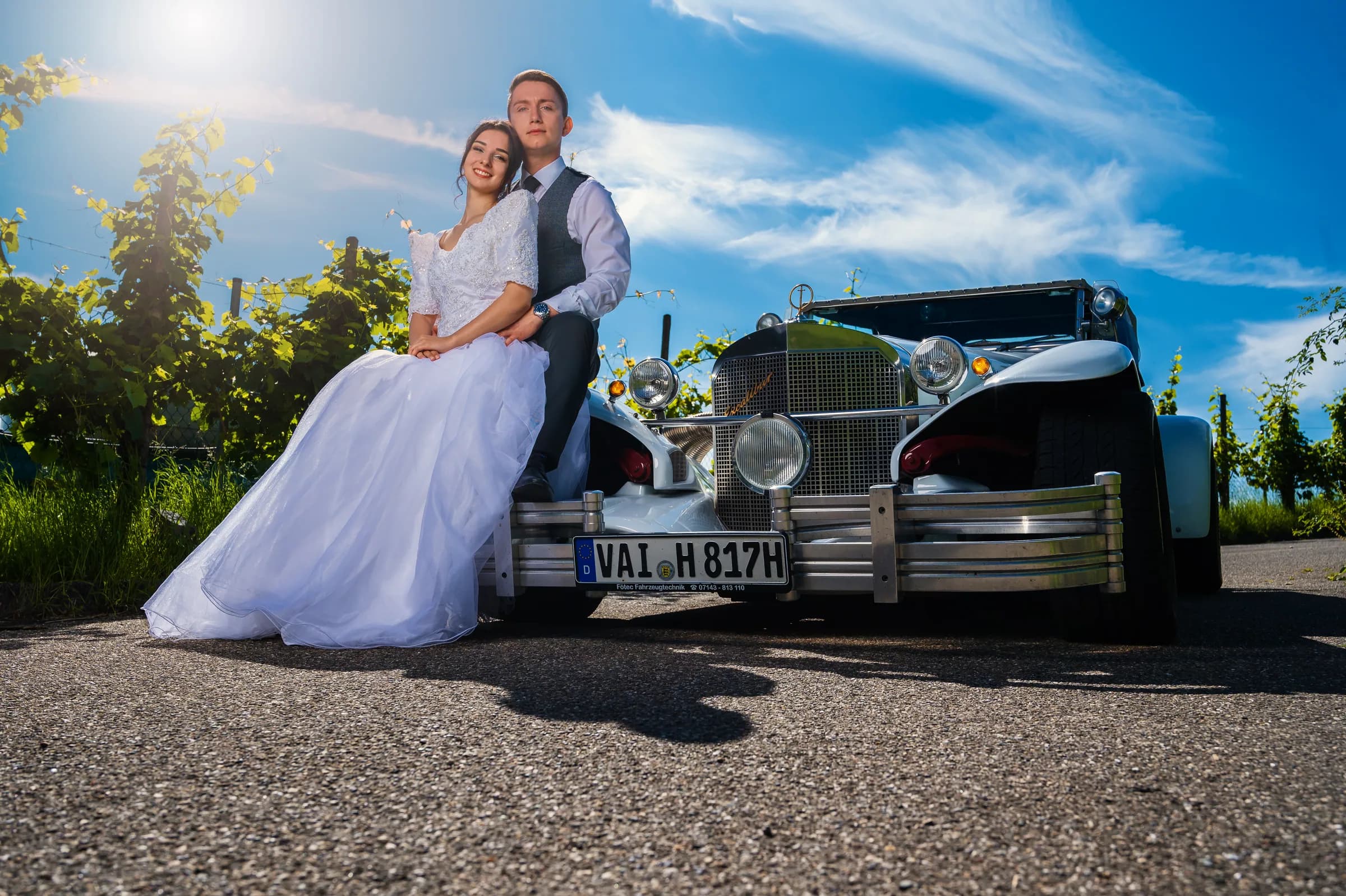 Brautpaar auf der Kühlerhaube eines Oldtimers zwischen Weinbergen