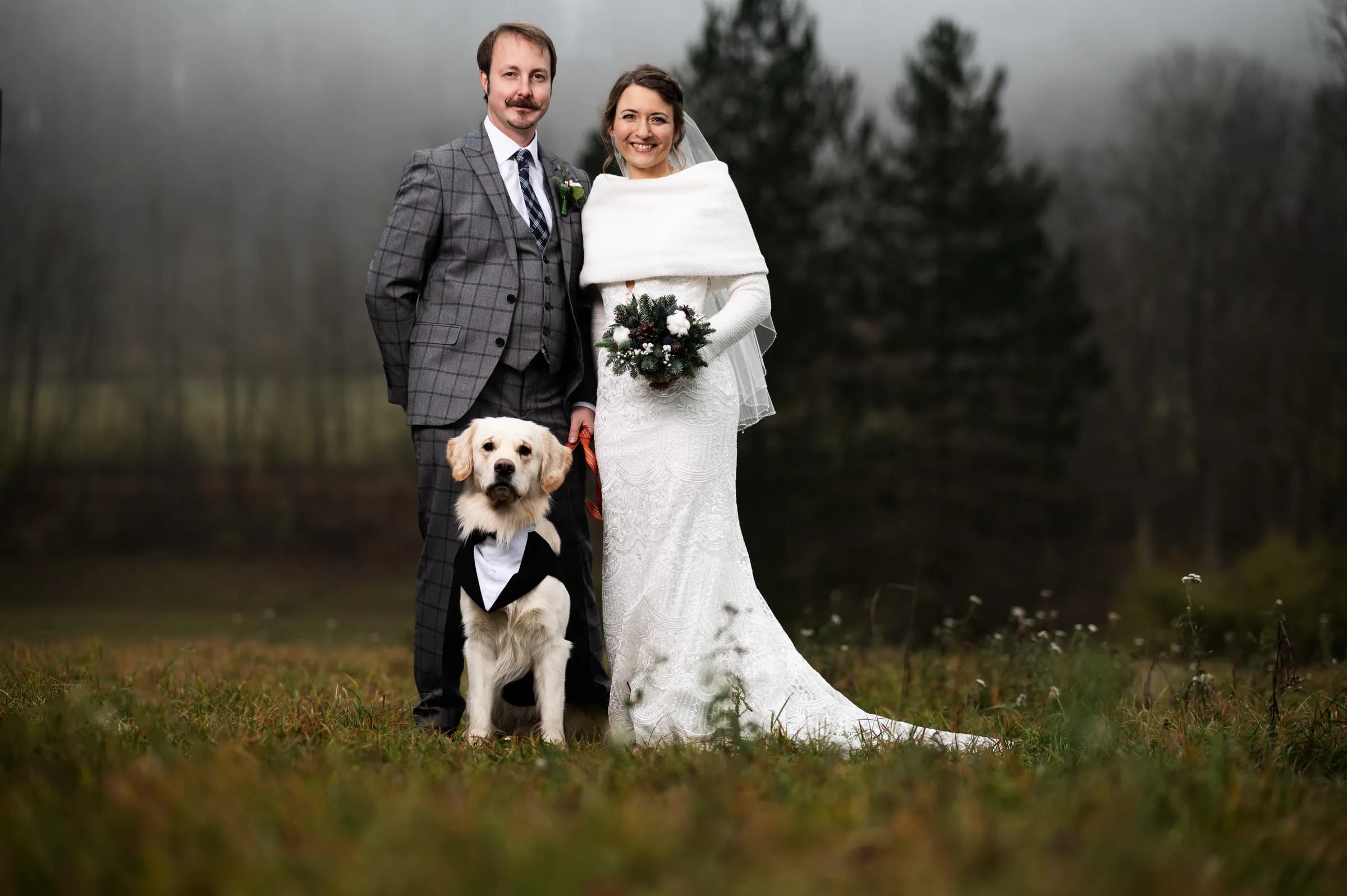 Brautpaar mit ihrem Labrador im Anzug auf einer Winterwiese