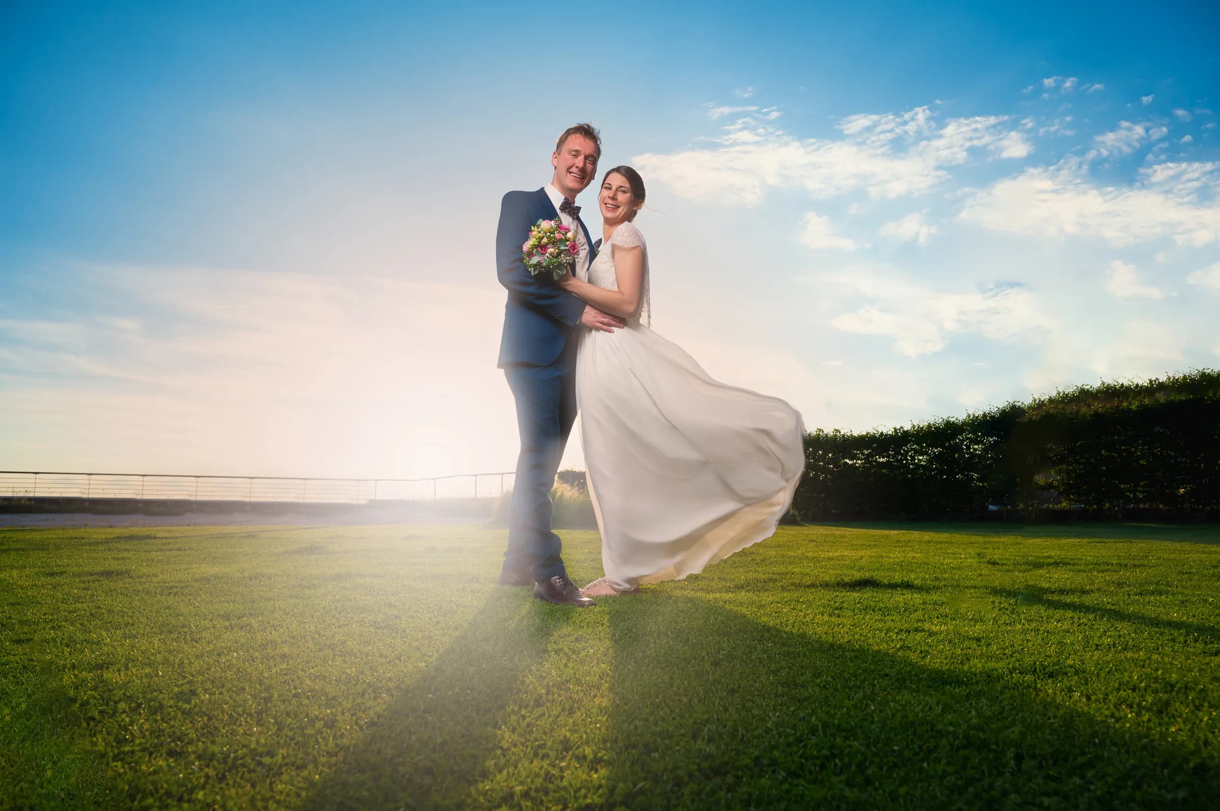 Brautpaar im Gegenlicht auf einer Wiese, Kleid im Wind
