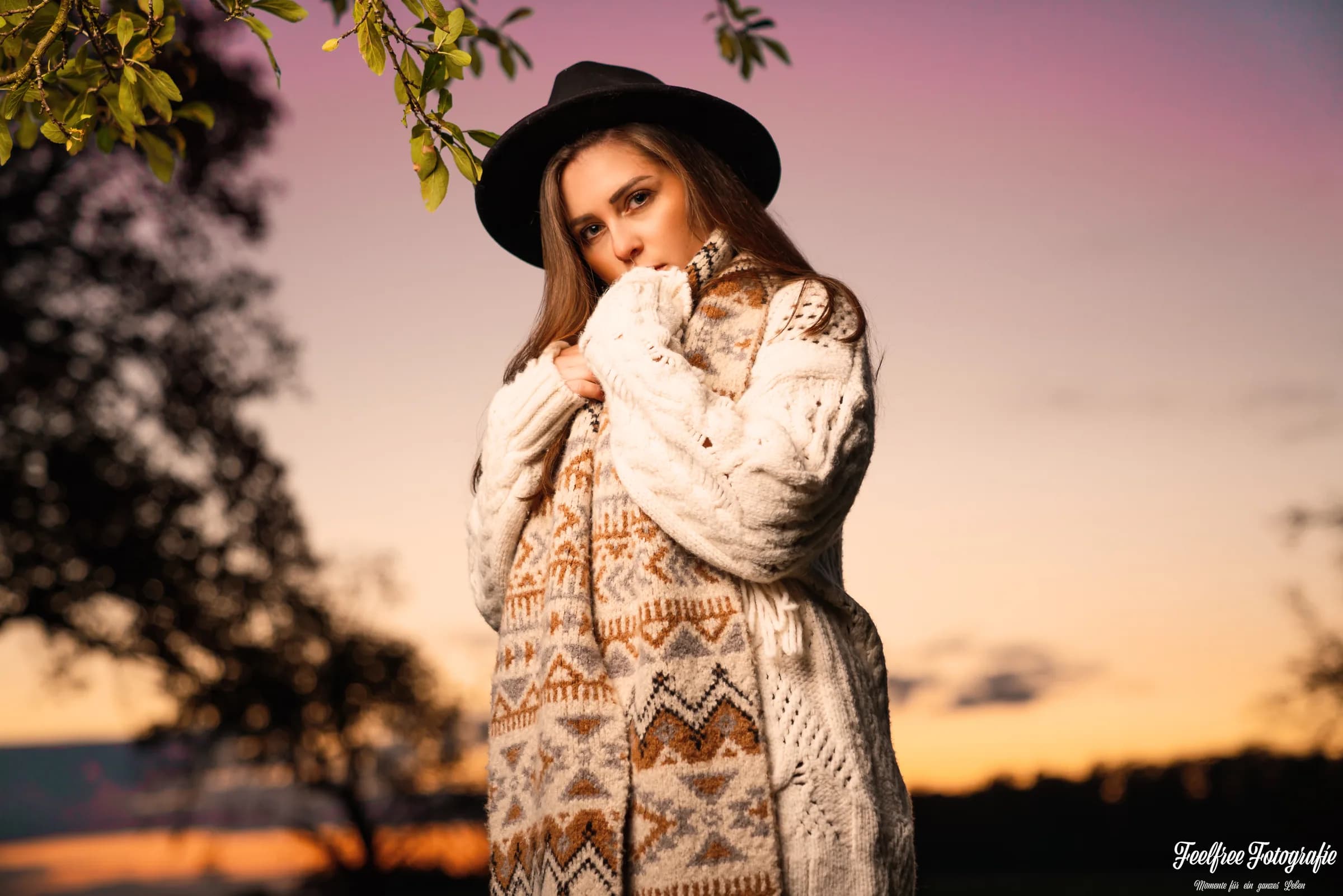 Junge Frau mit Hut und Strickjacke vor rosa Abendhimmel