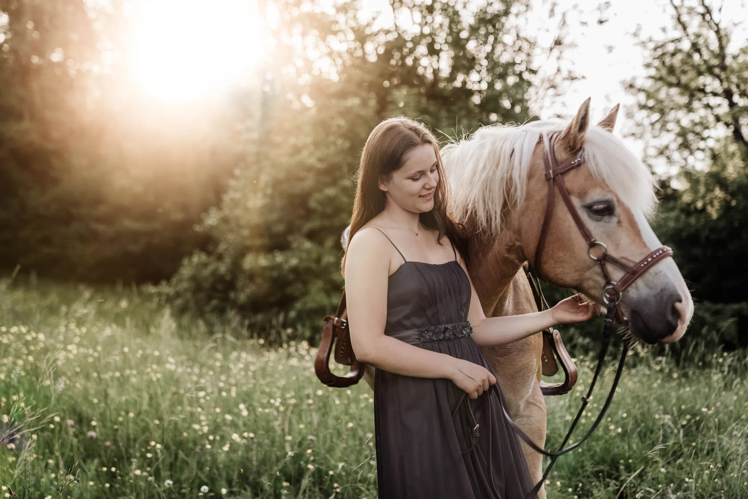 Junge Frau führt ihren Haflinger über eine Blumenwiese im Gegenlicht